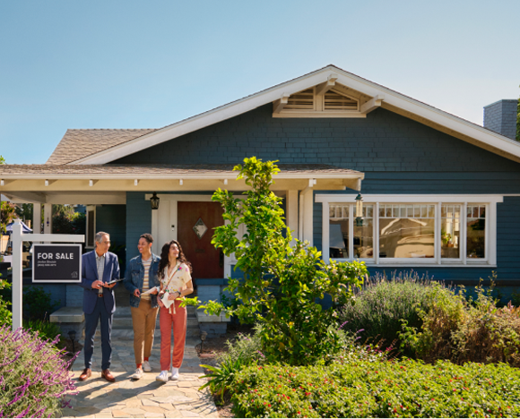 three people standing in front of house with for sale sign