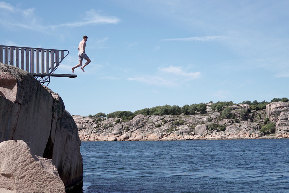 man jumping off high dive into lake