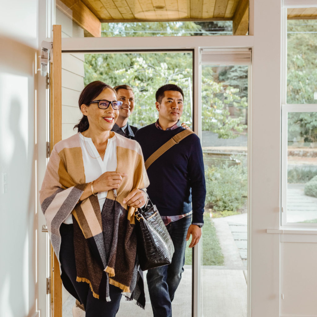 Female real estate agent walks into the front entry of a house with her clients, a couple, behind her