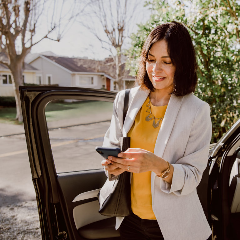 Real estate agent checking her mobile phone after she gets out of a car