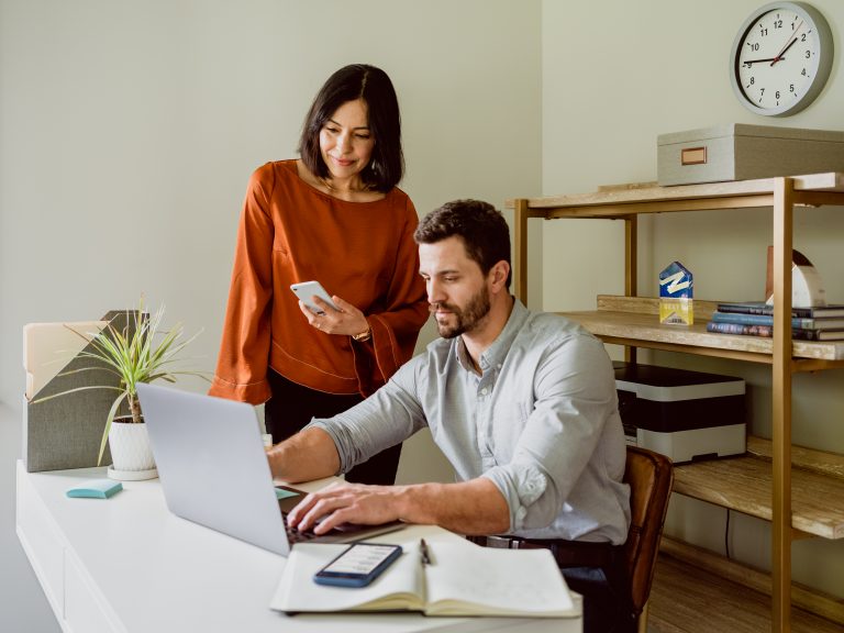 Two real estate agents in an office looking at information on a laptop screen