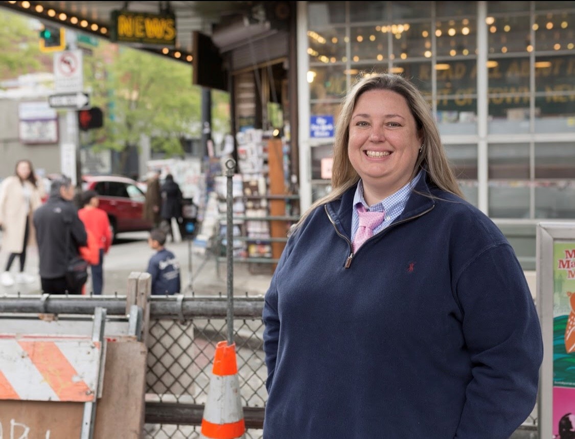 Snapshot of Zillow employee Brenna Penrod. She's wearing a navy blue zip-up sweatshirt and is standing in front of a news stand surrounded by construction cones at Seattle's Pike Place Market.