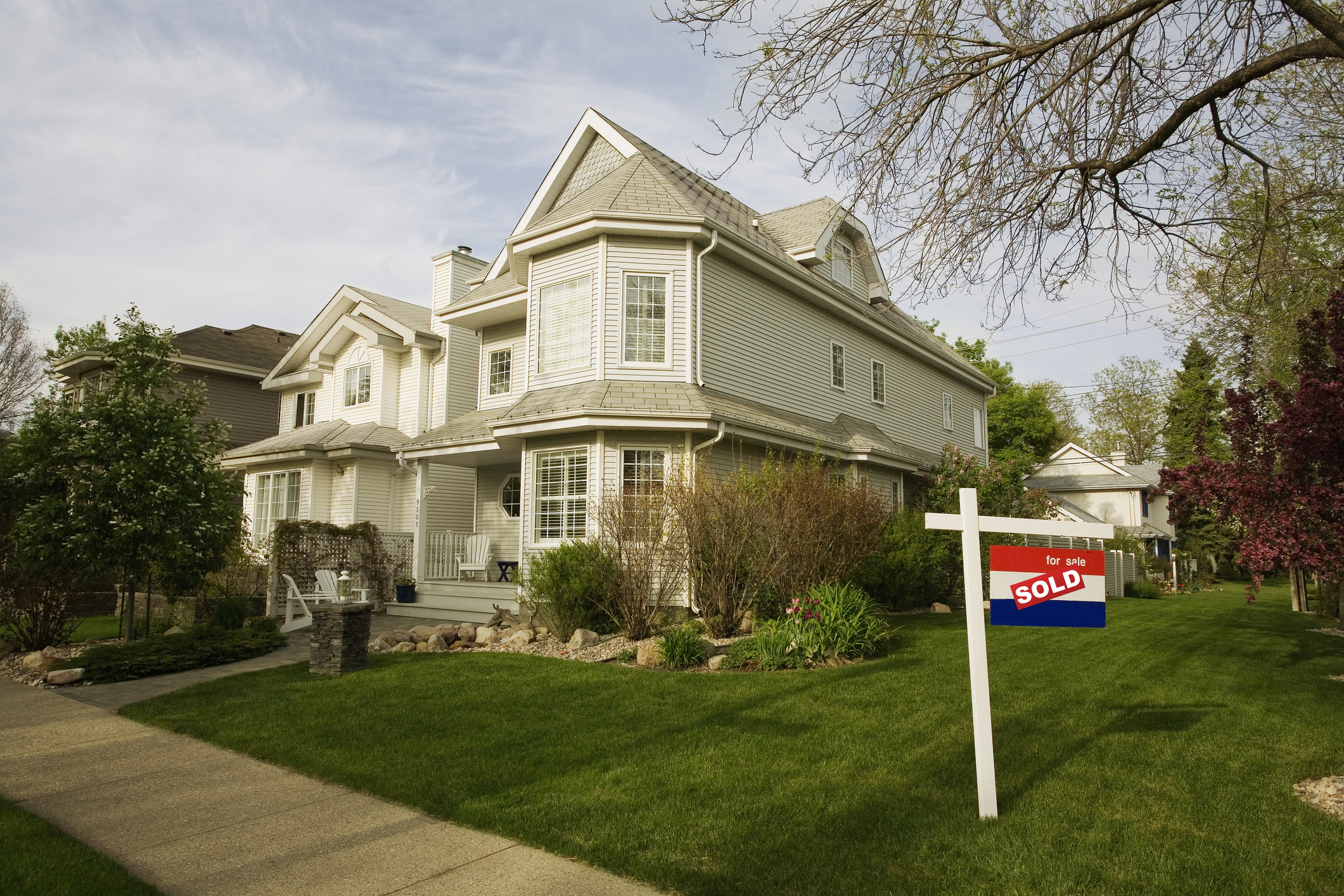 White house with a for sale sign that has a 'sold' sticker over top of it