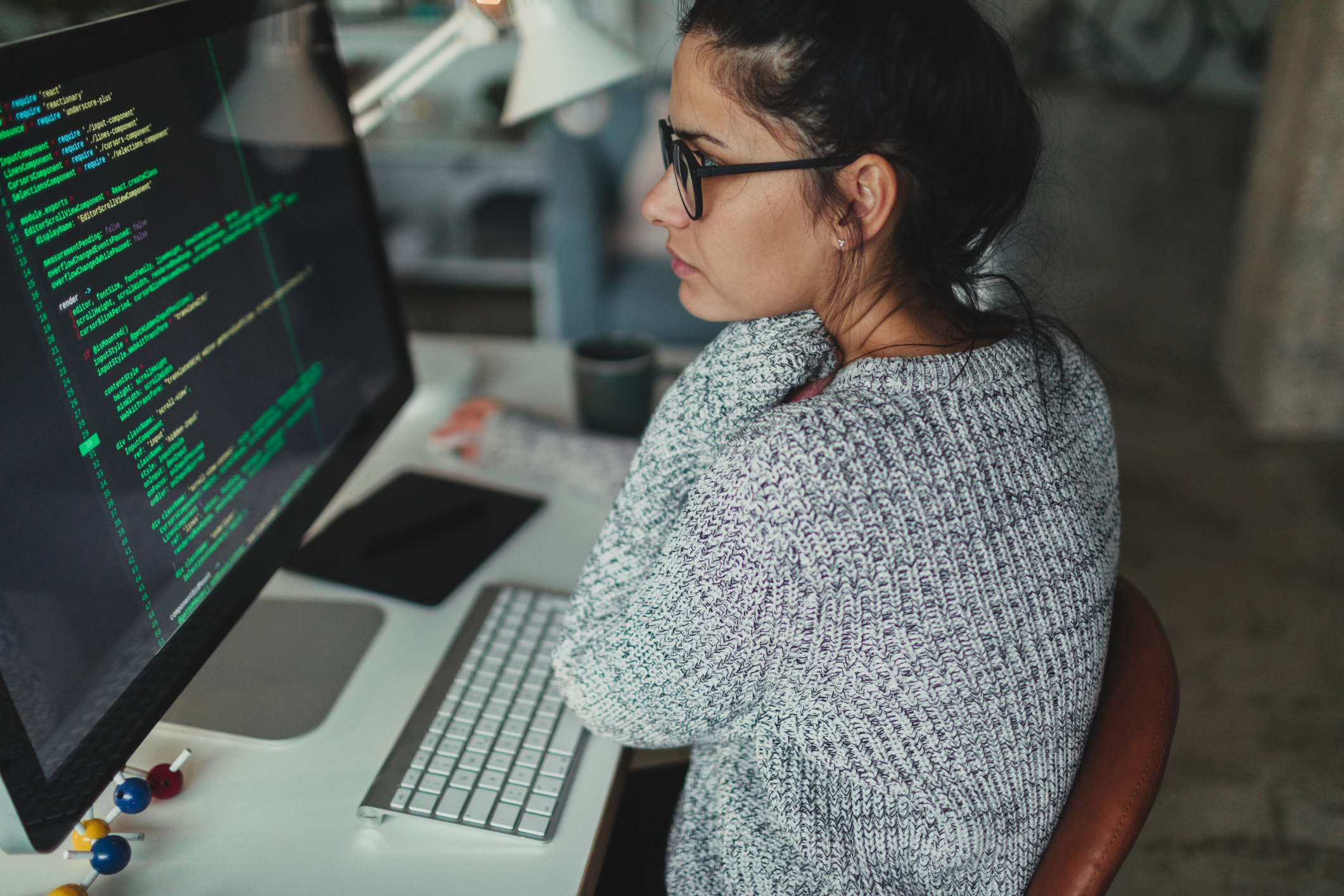 Photo of a young woman sitting at her desktop computer, doing computer programming in her home office