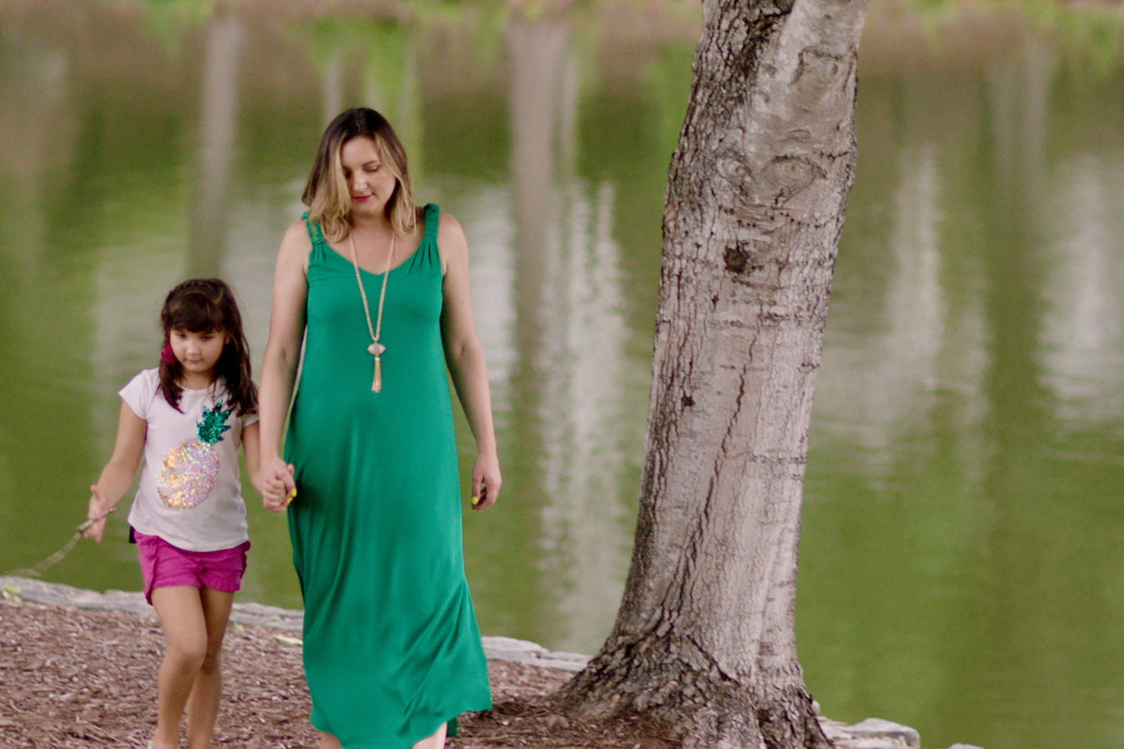 Woman holding child's hand as they walk alongside a lake