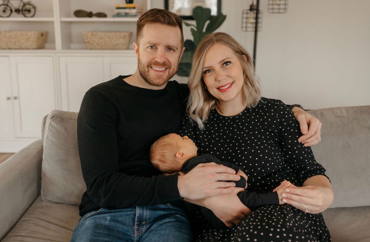 portrait of mother and father sitting on a couch holding their newborn son