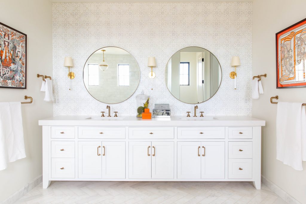 a bathroom with a white antique-looking bureau with sinks mounted in it and circle-shaped mirrors on the wall