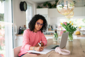 woman writing next to laptop in kitchen - for sale by owner (FSBO)