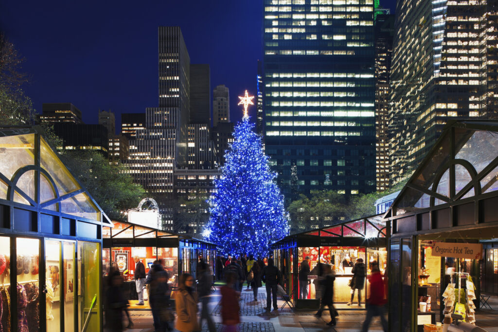 Large Christmas tree lit up blue behind stalls at Bryant Park Winter Village holiday market nyc
