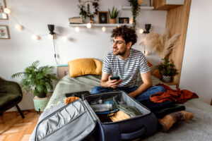 man sits on bed with open suitcase - prepare nyc apartment before traveling