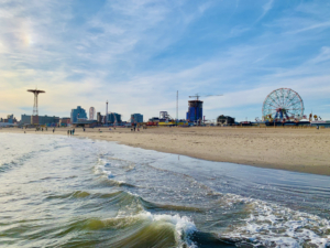 waves lap against Coney Island beach with ferris wheel in background