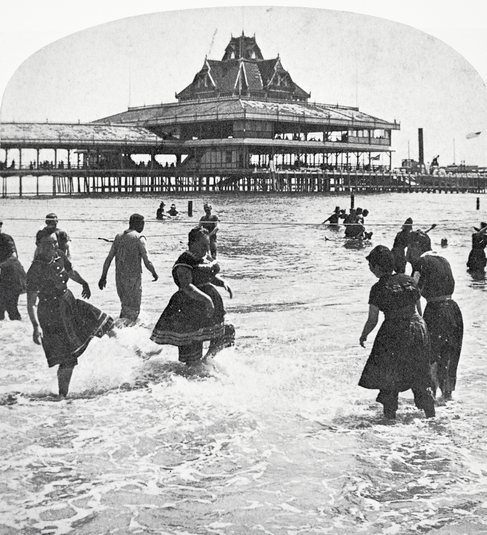 Black-and-white image of people wadding into the ocean near Iron Steamboat Pier, Coney Island, 1889