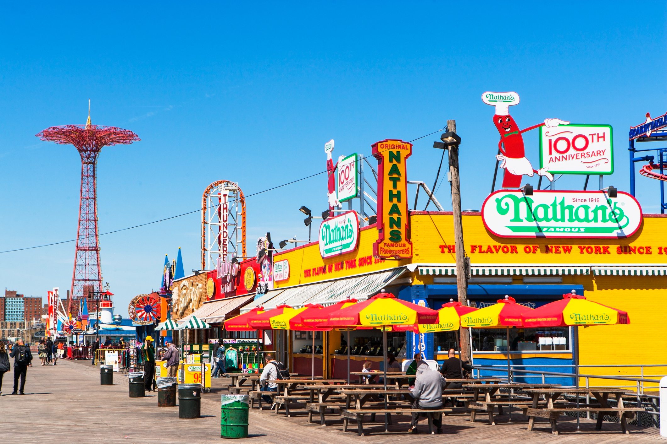Iconic Nathan's Famous Hot Dogs on the Coney Island boardwalk with amusement park rides in the background