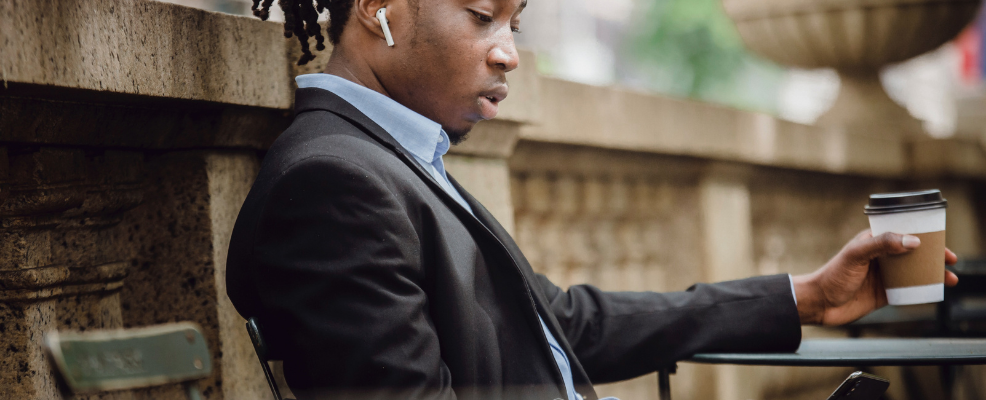 Person outside with coffee and headphones looking down at phone