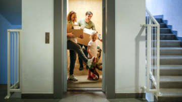 Family with one child moves with boxes with dog and toy dinosaur on elevator to new apartment.