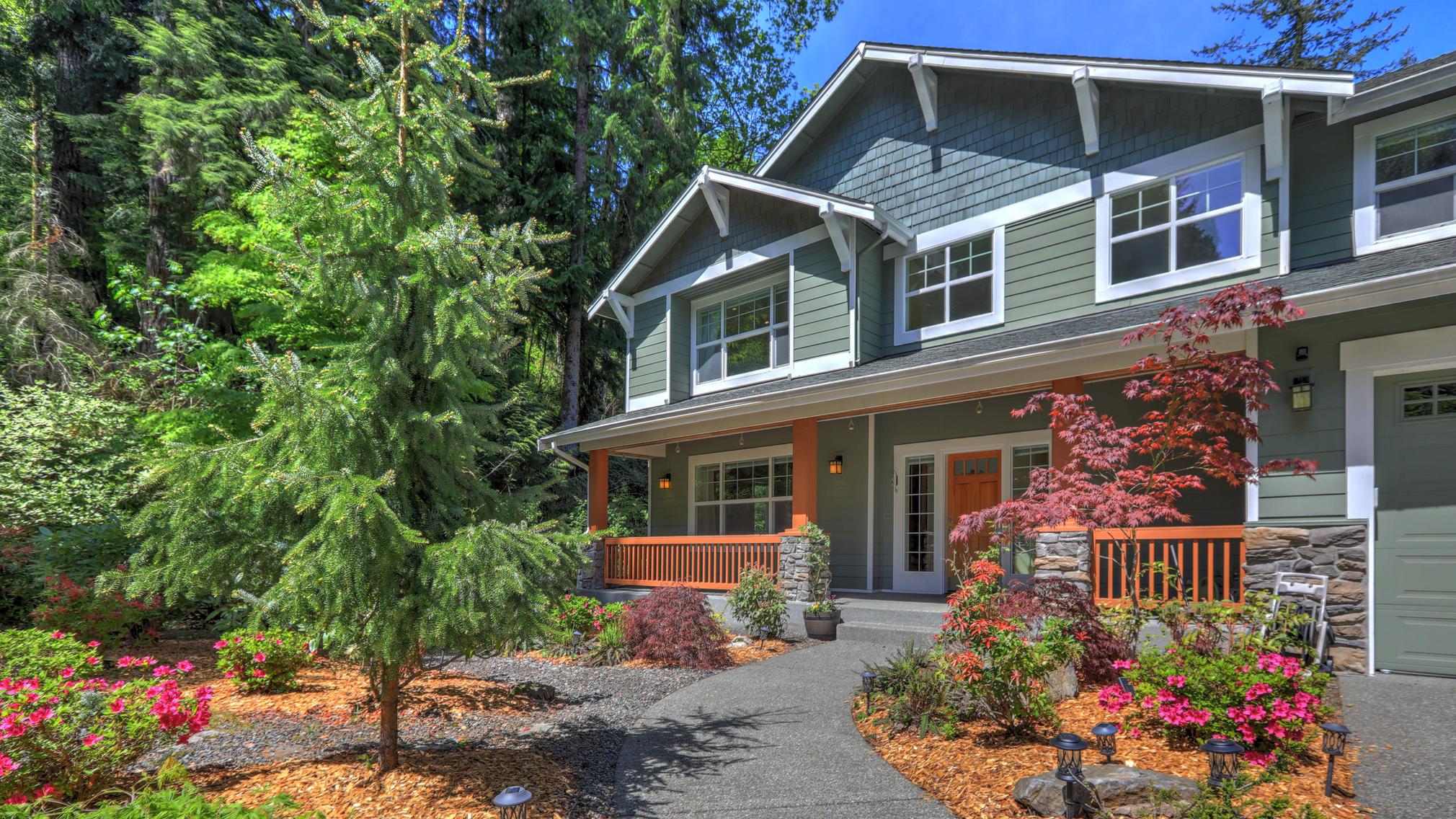 Beautiful two story tall Northwest Home Exterior in grey green with spring landscaping and large driveway, garden and large pond fountain with rocks.