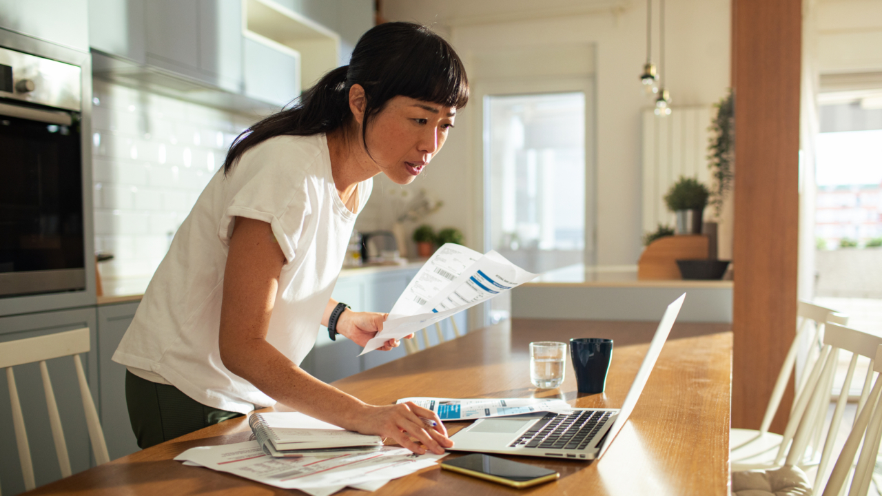 woman working in kitchen, standing over her laptop.