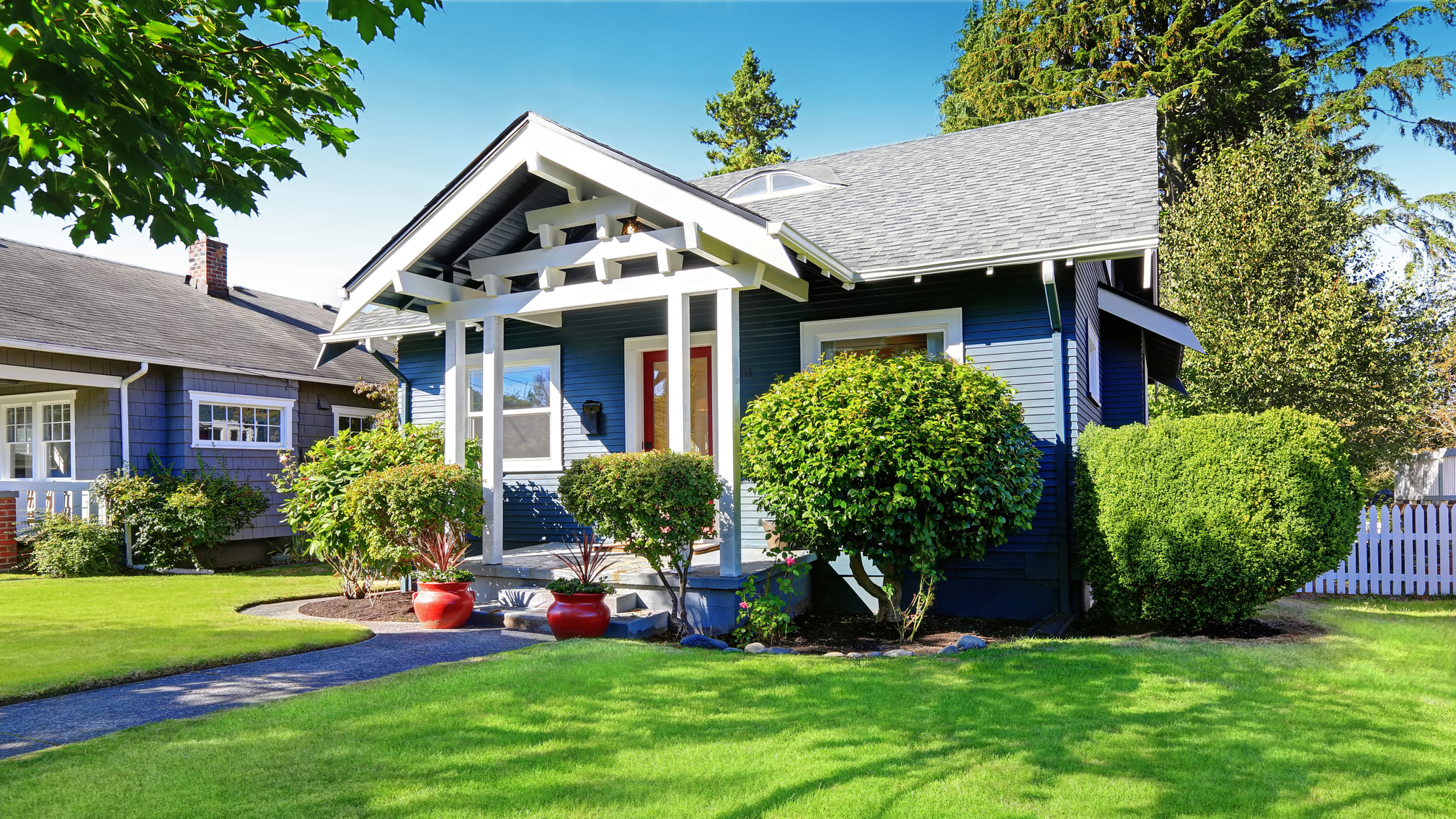 Blue and white single family home exterior with red pots and a green lawn.