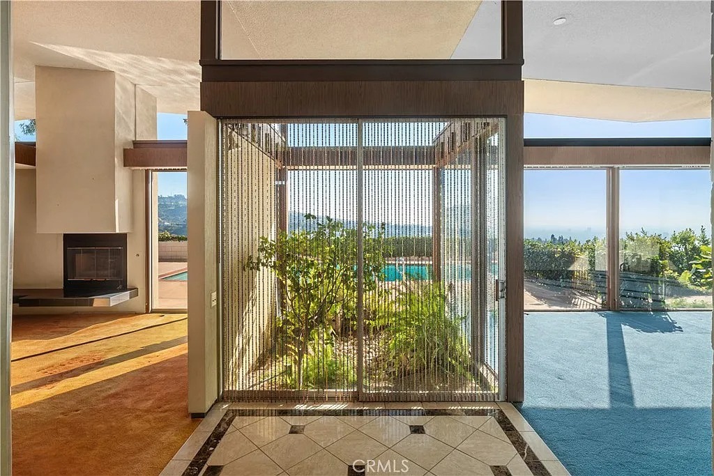 The space age interior design of this home features a unique indoor garden surrounded by large windows offering a scenic outlook. The architectural choices capture the optimism and style of mid-century modernism entwined with the future.