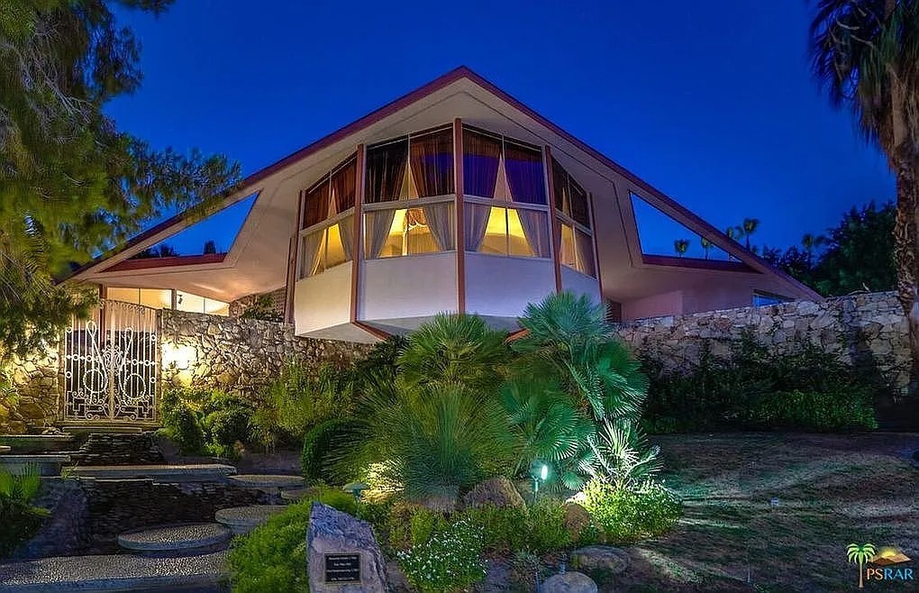 This space age residence, set against a backdrop of night, boasts a dramatic roofline reminiscent of a mid-century modern spacecraft. Large windows illuminate the interior, suggesting an innovative living space.