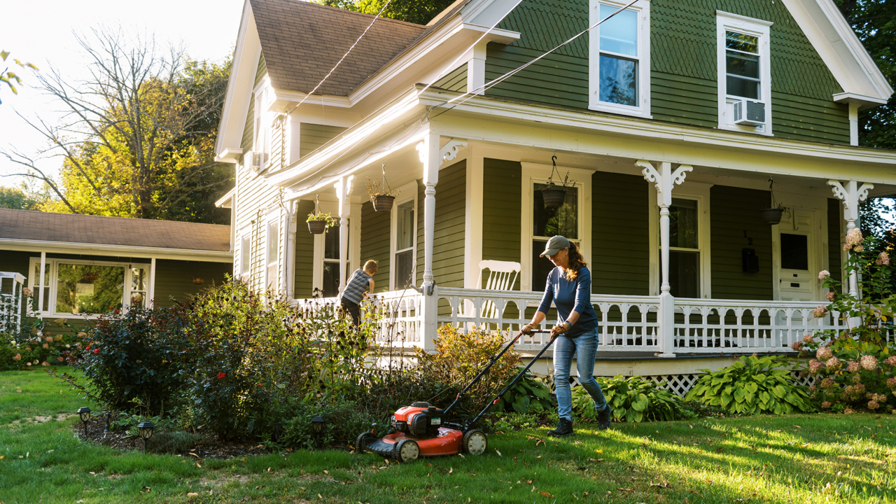 Woman mowing the lawn as part of home maintenance. A lawn service is just one of many annual home maintenance costs homeowners may have to budget for.