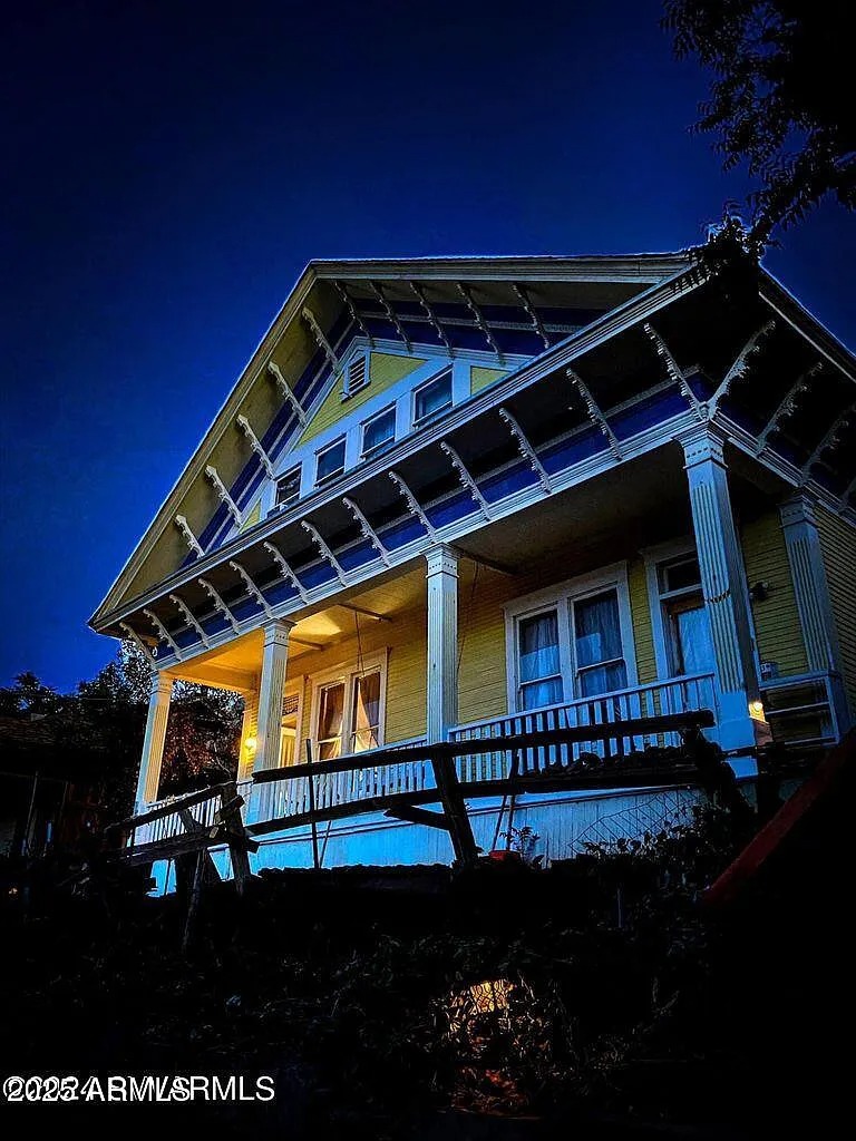 A yellow, Victorian duplex is photographed just after sunset, from a low-to-the-ground perspective.