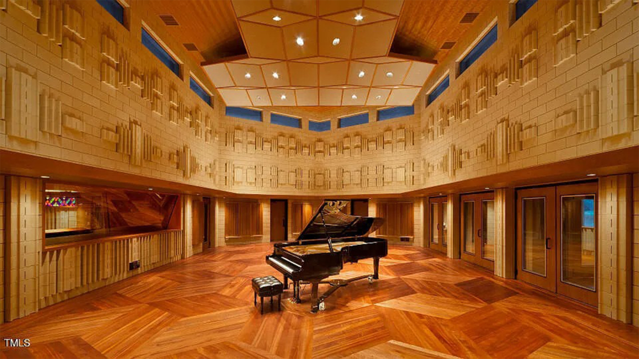 A grand piano sits in the center of a large music recording space.