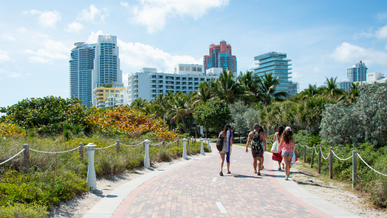 A paved walking path with three people on it and the Miami skyline in the distance.