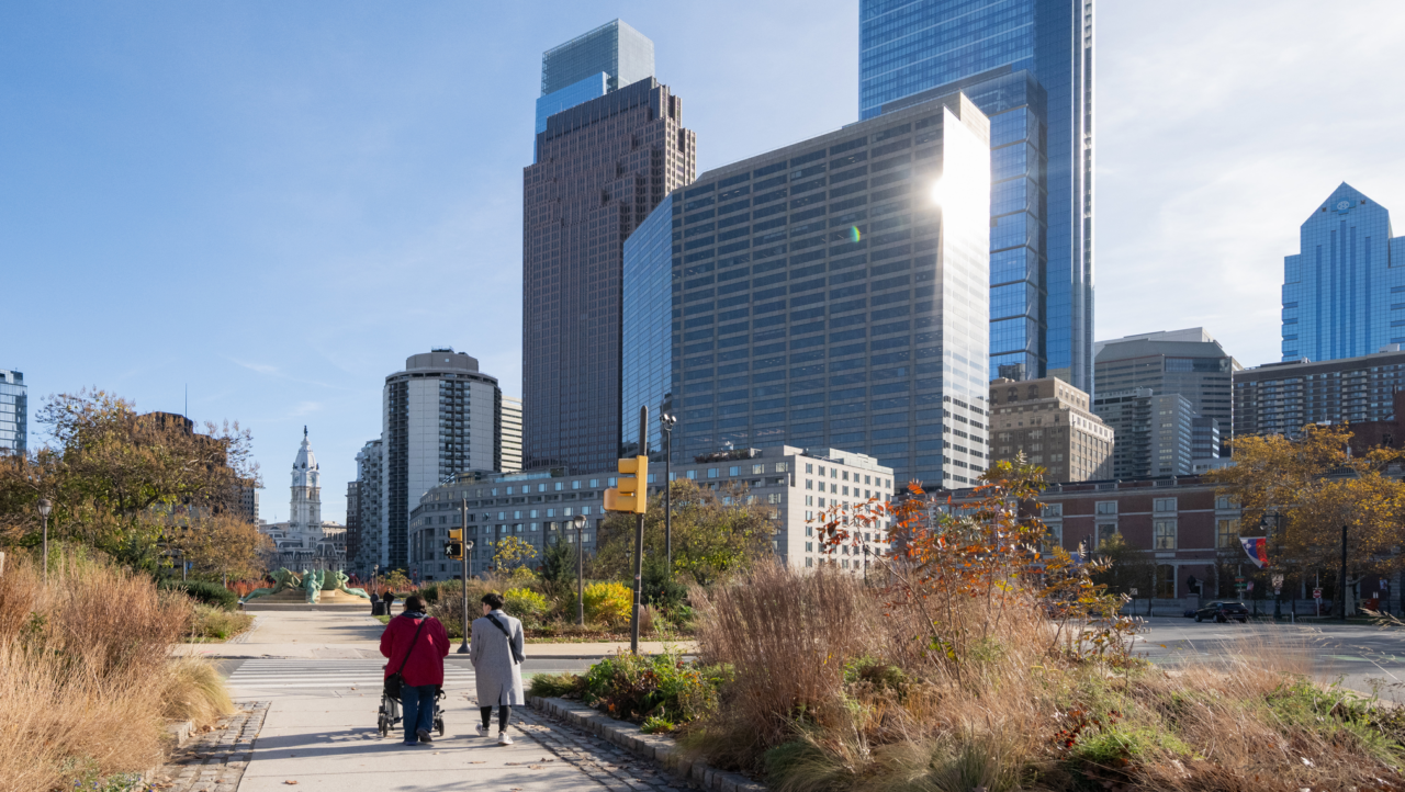 Looking at tall buildings in Philadelphia from a walking path, with people in the foreground.