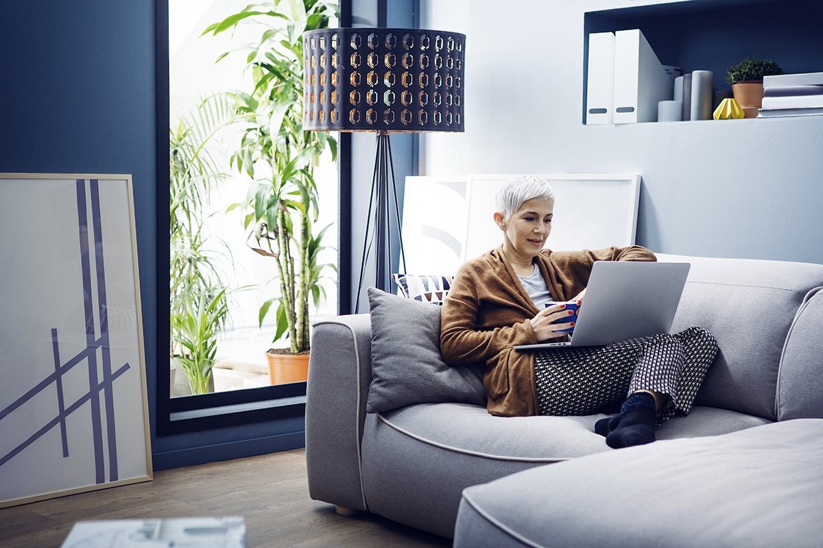 Woman reclining on a sofa with a cup of coffee and a laptop