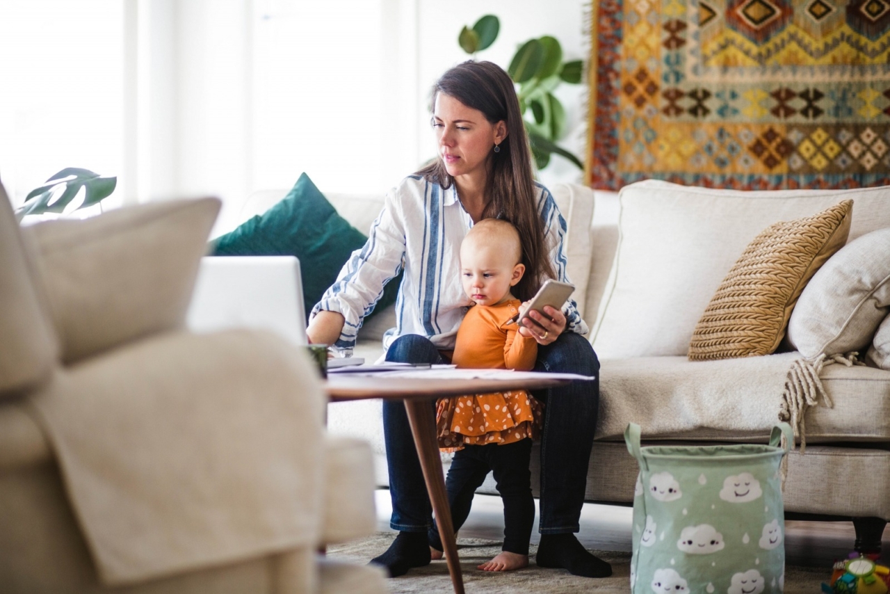 Woman holding phone with her child while on computer