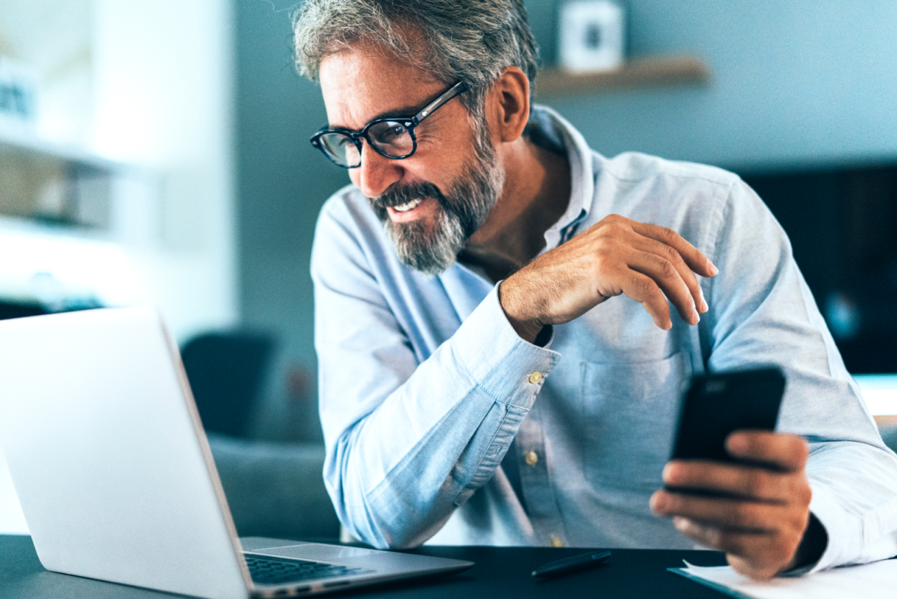 Man holding cell phone and smiling at his open laptop