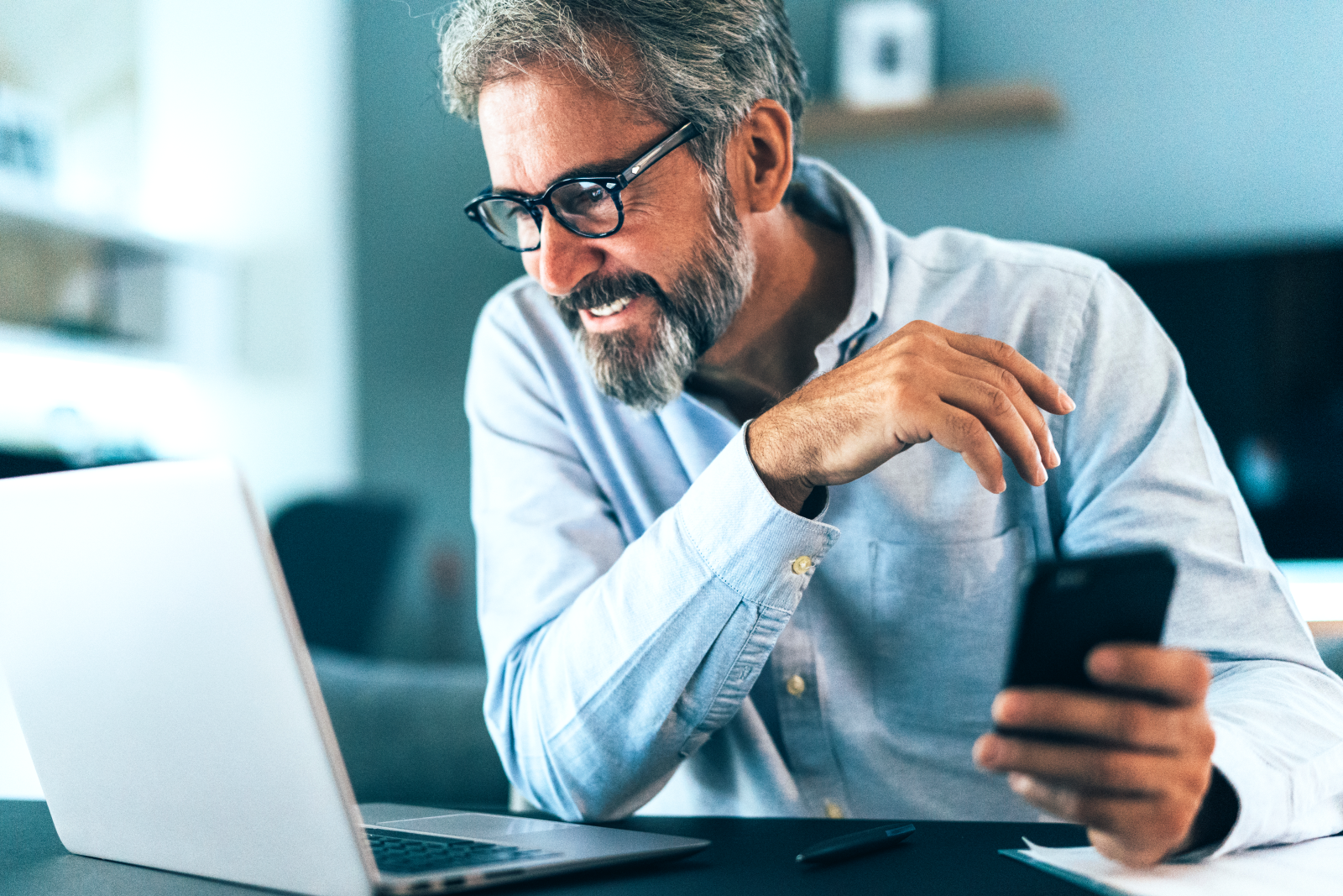 Man holding cell phone and smiling at his open laptop