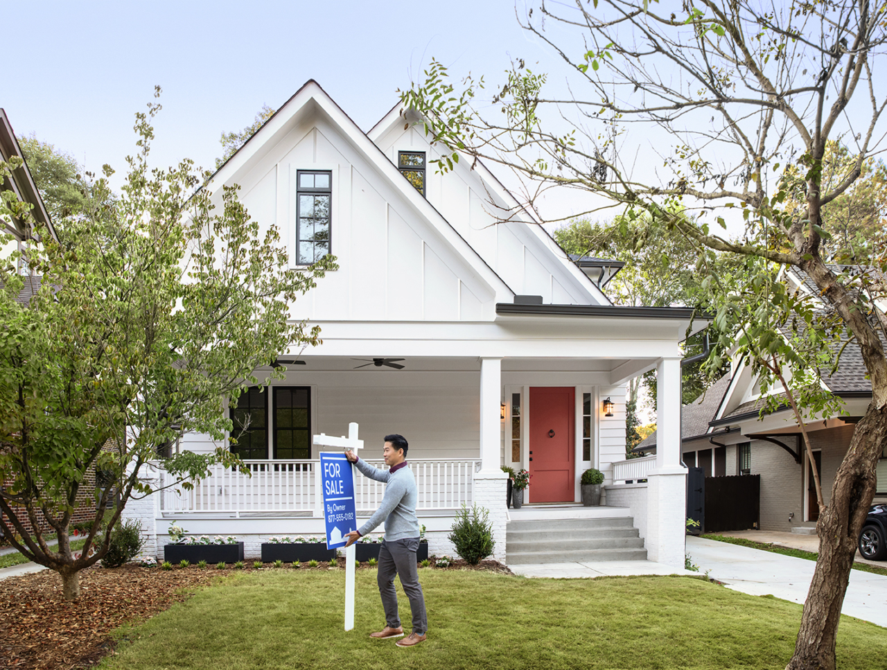 A person adjusting a for sale sign outside a home