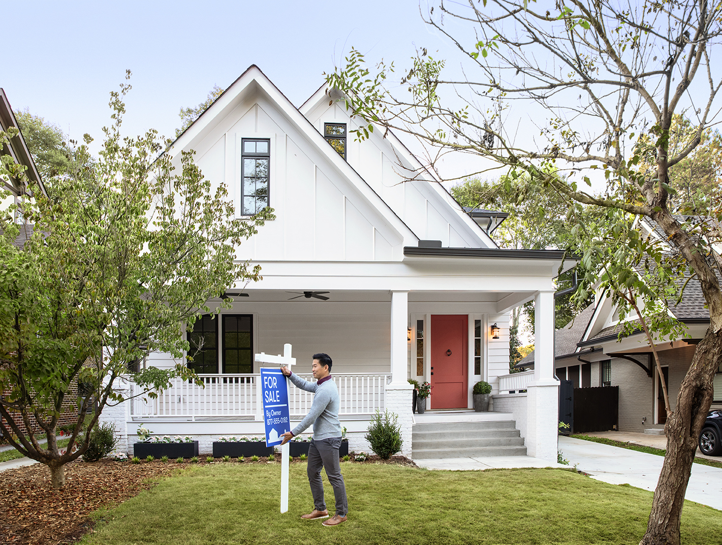 A person adjusting a for sale sign outside a home