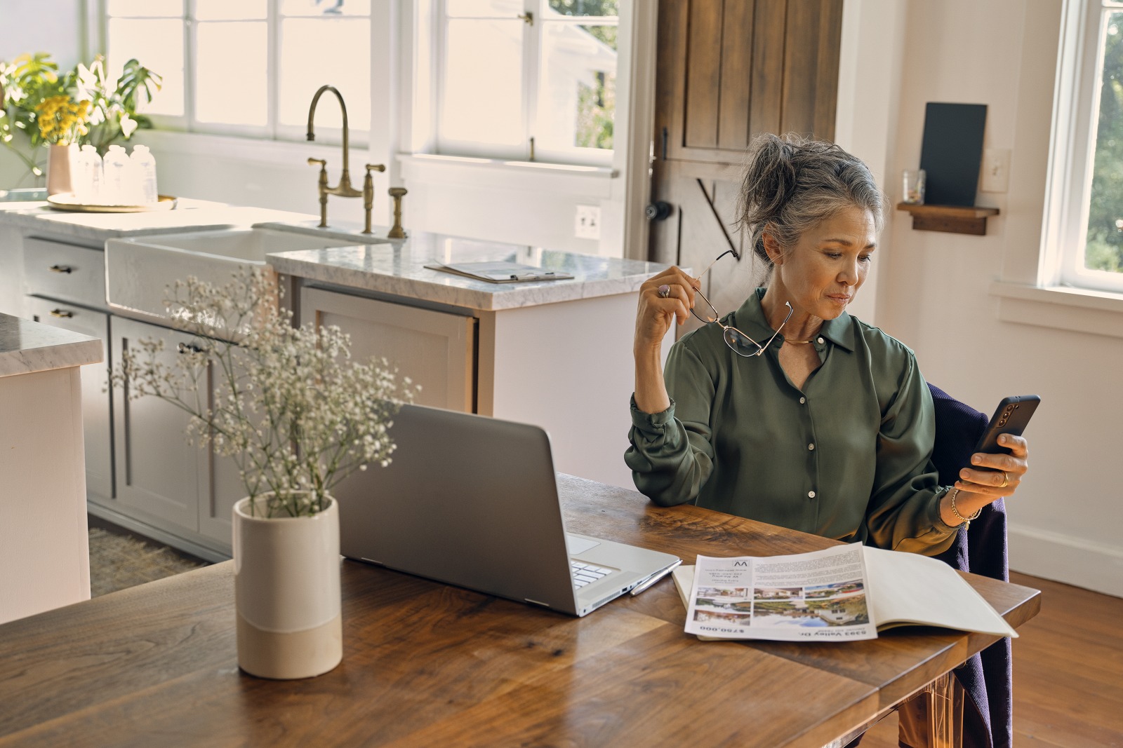Image depicts a woman sitting at a table and looking at a smart phone