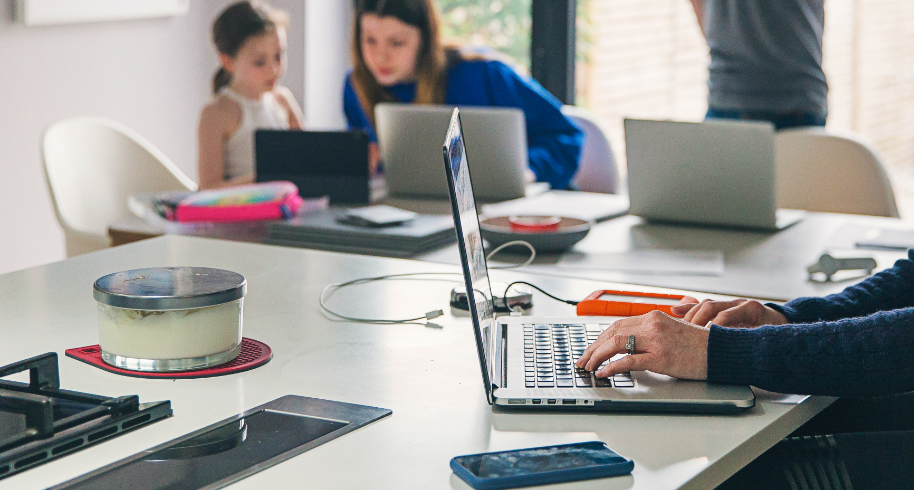 Person working from home in the foreground with children and parents on computers in the background.