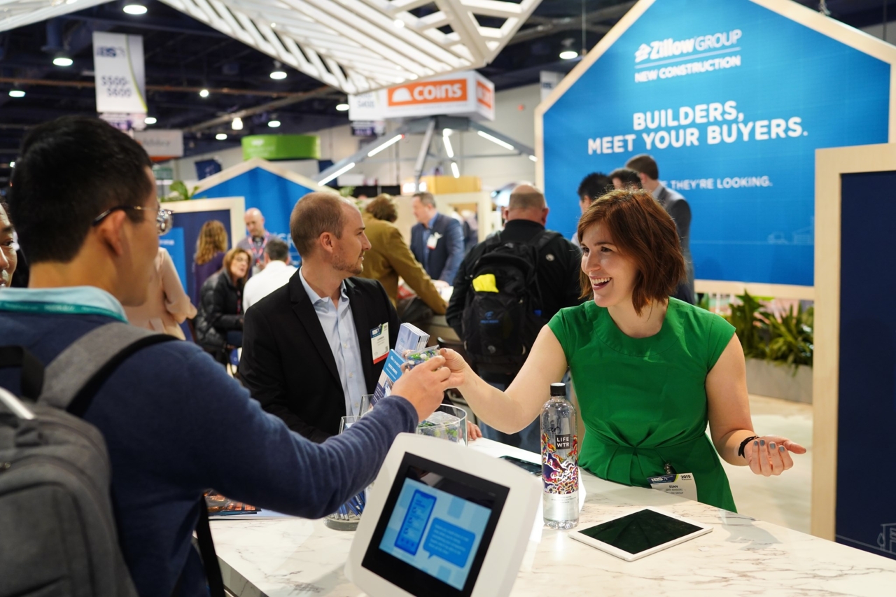 Image depicts two people exchanging swag at a Zillow booth during the IBS conference.
