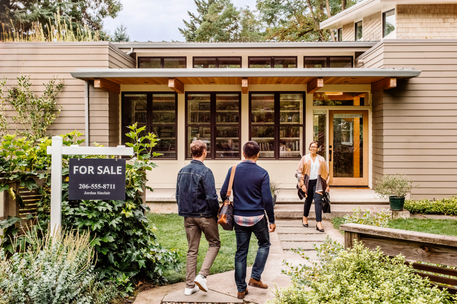 Two people meeting an agent in front of a home for sale to learn about a career in real estate.
