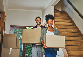 Couple walking into their new home carrying boxes.
