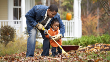 black homeowner raking leaves in yard with child