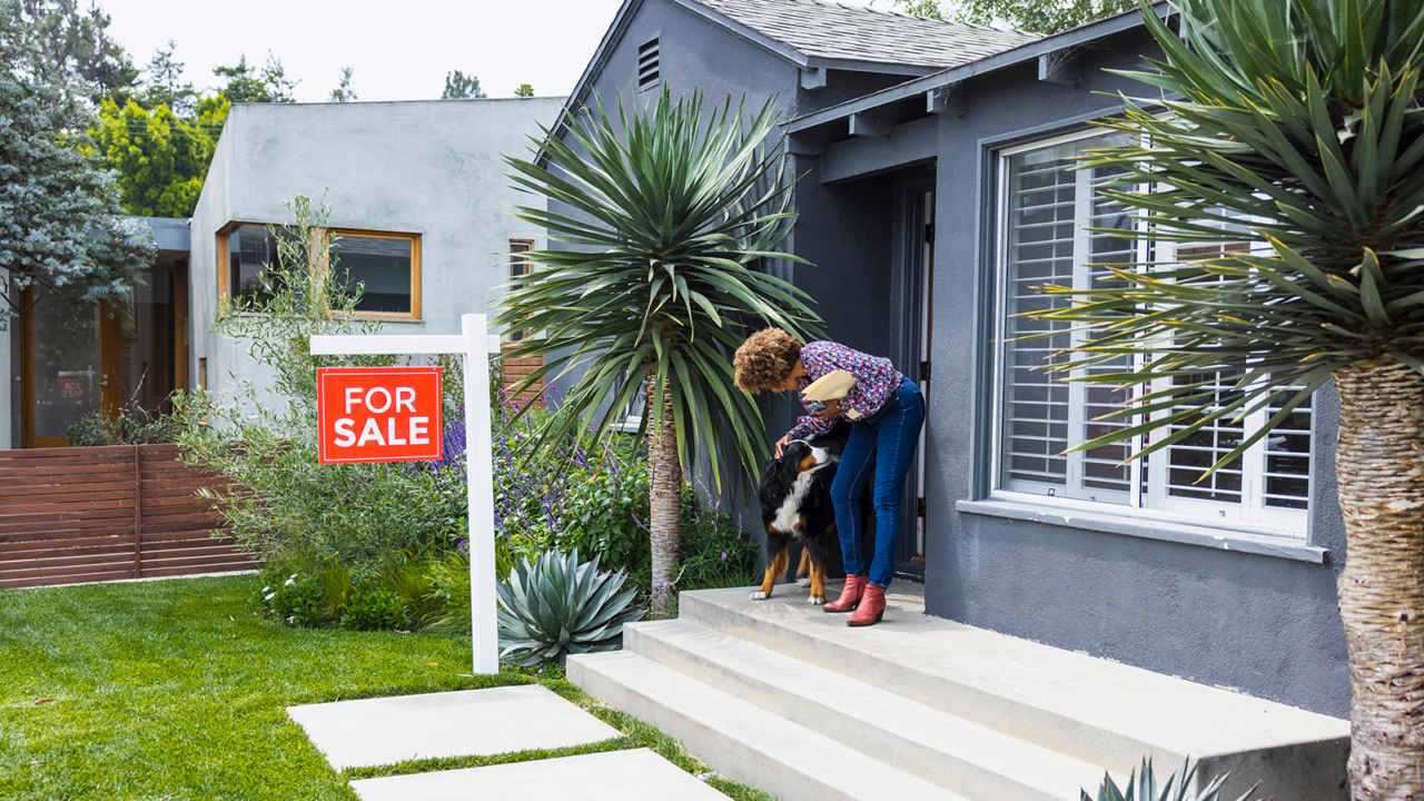 person outside of house with a for sale sign