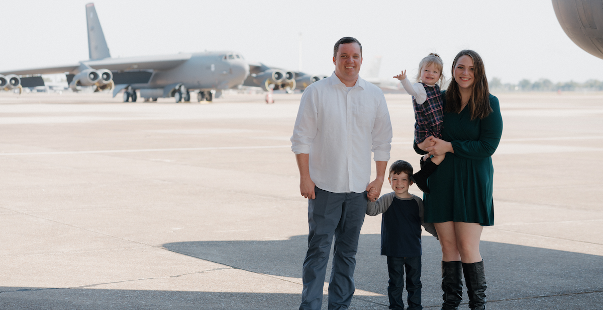 Christine with her husband and two children pose in front of a military aircraft.